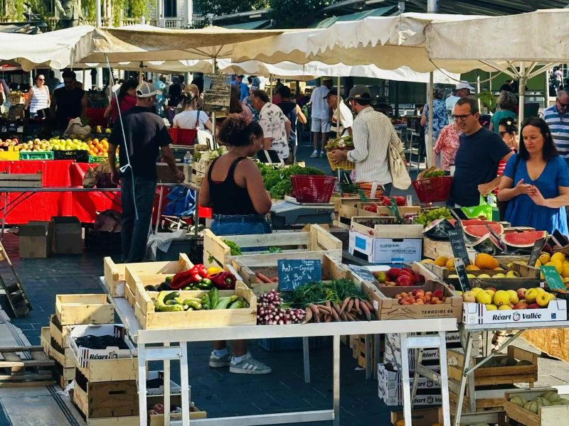 Busy market scene showcasing vibrant fruits and vegetables at Nice's Marché de la Libération under sunny skies.