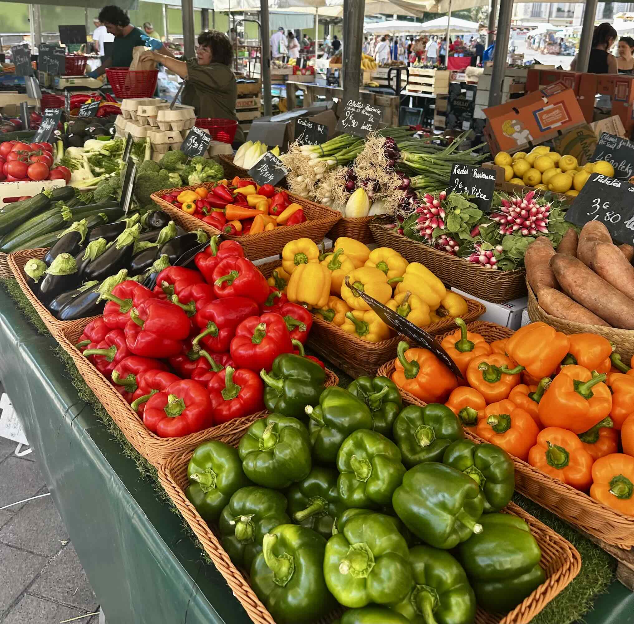 Vibrant display of fresh vegetables including bell peppers, zucchini, and radishes at Marché de la Libération in Nice.