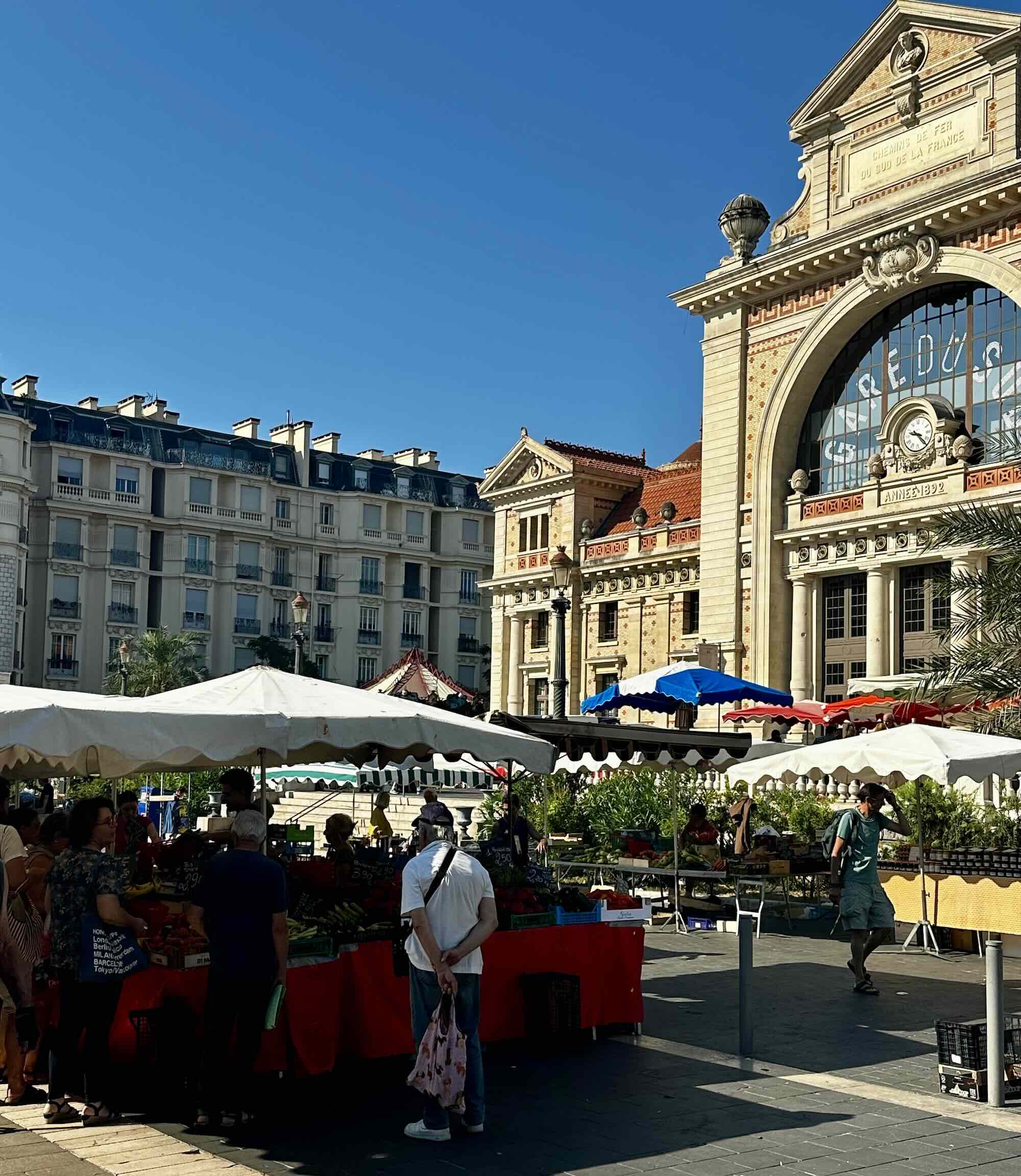 A bustling market scene at Marché de la Libération in Nice, featuring colorful stalls and shoppers enjoying the vibrant atmosphere.