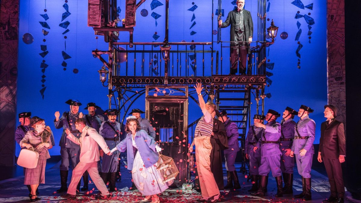 A lively scene from Il Barbiere di Siviglia, featuring performers in colorful costumes amid a burst of petals.