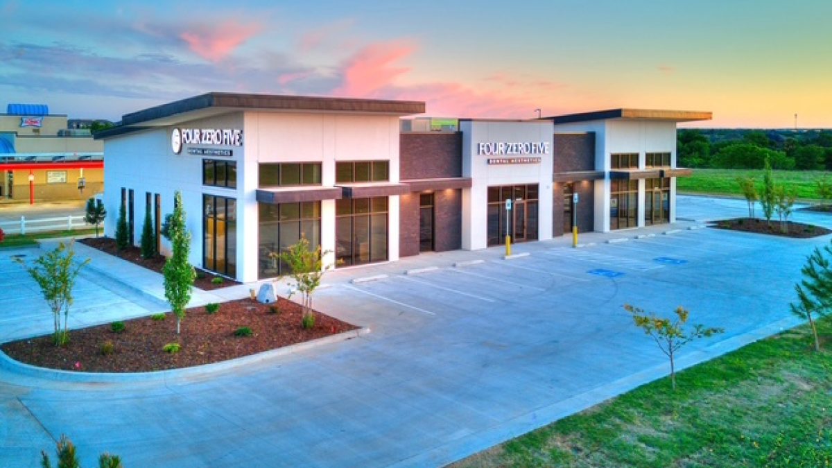 Modern dental building with large windows, signage, and a spacious parking lot during sunset.