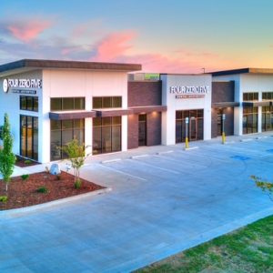 Modern dental building with large windows, signage, and a spacious parking lot during sunset.