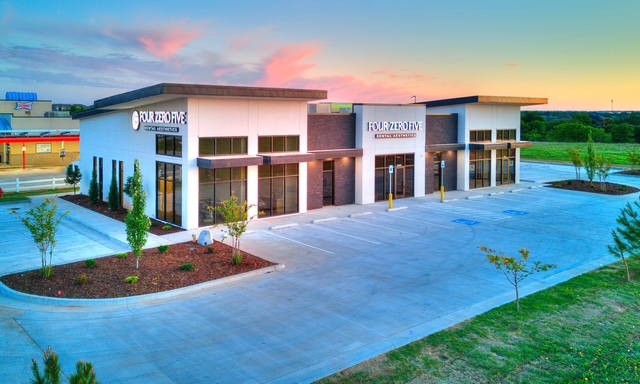 Modern dental building with large windows, signage, and a spacious parking lot during sunset.