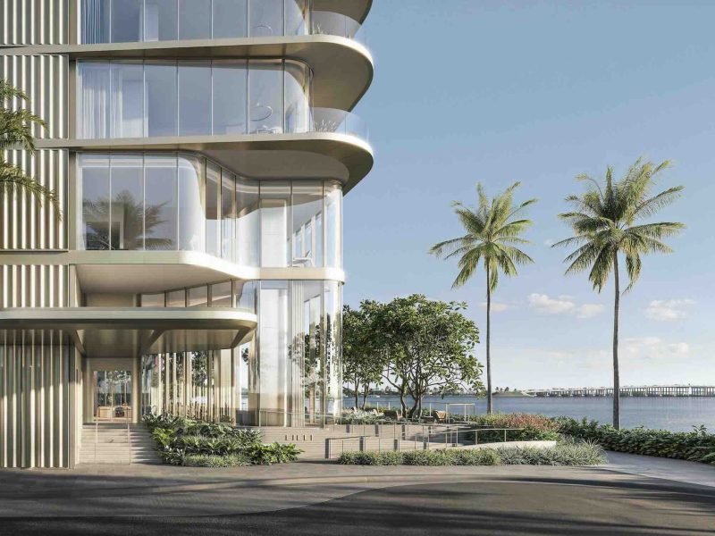 Modern luxury waterfront building entrance with palm trees and a view of the water in Miami.