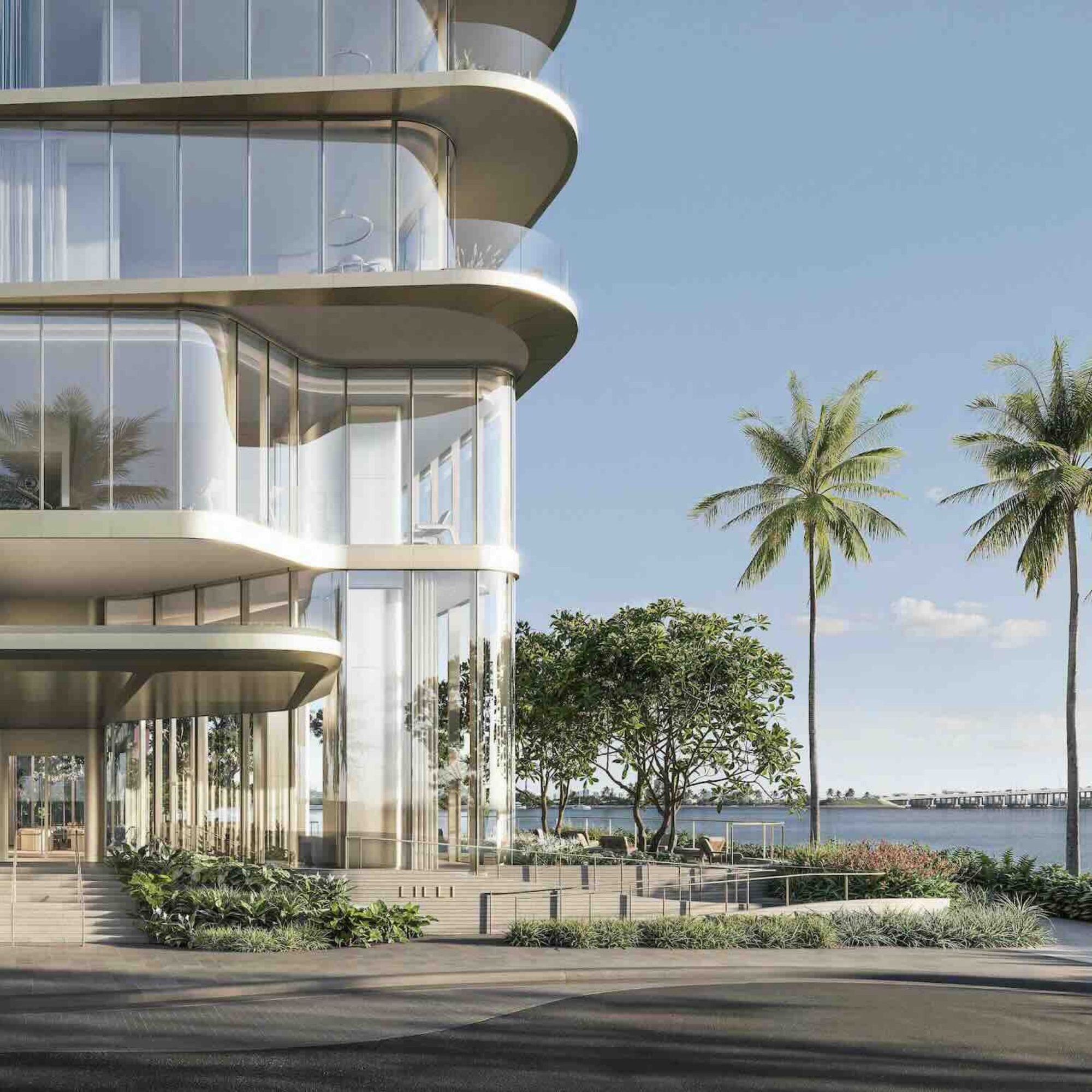 Modern luxury waterfront building entrance with palm trees and a view of the water in Miami.