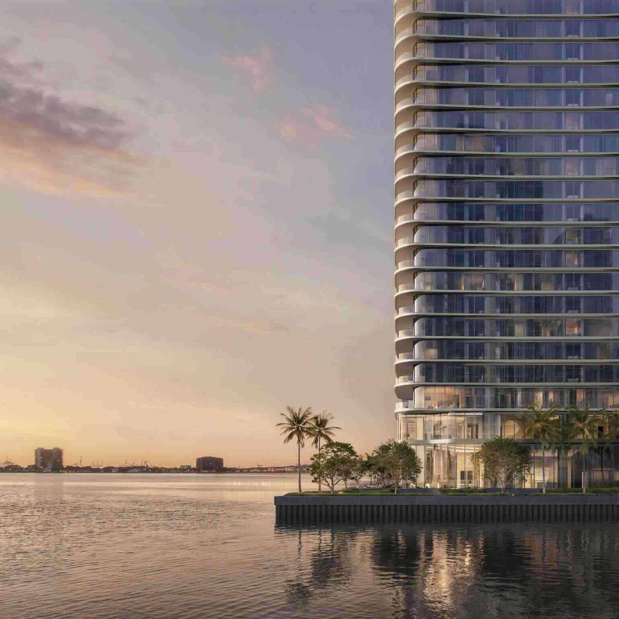 Modern waterfront building with glass exterior, palm trees, and sunset reflections on the water, symbolizing luxury in Miami.