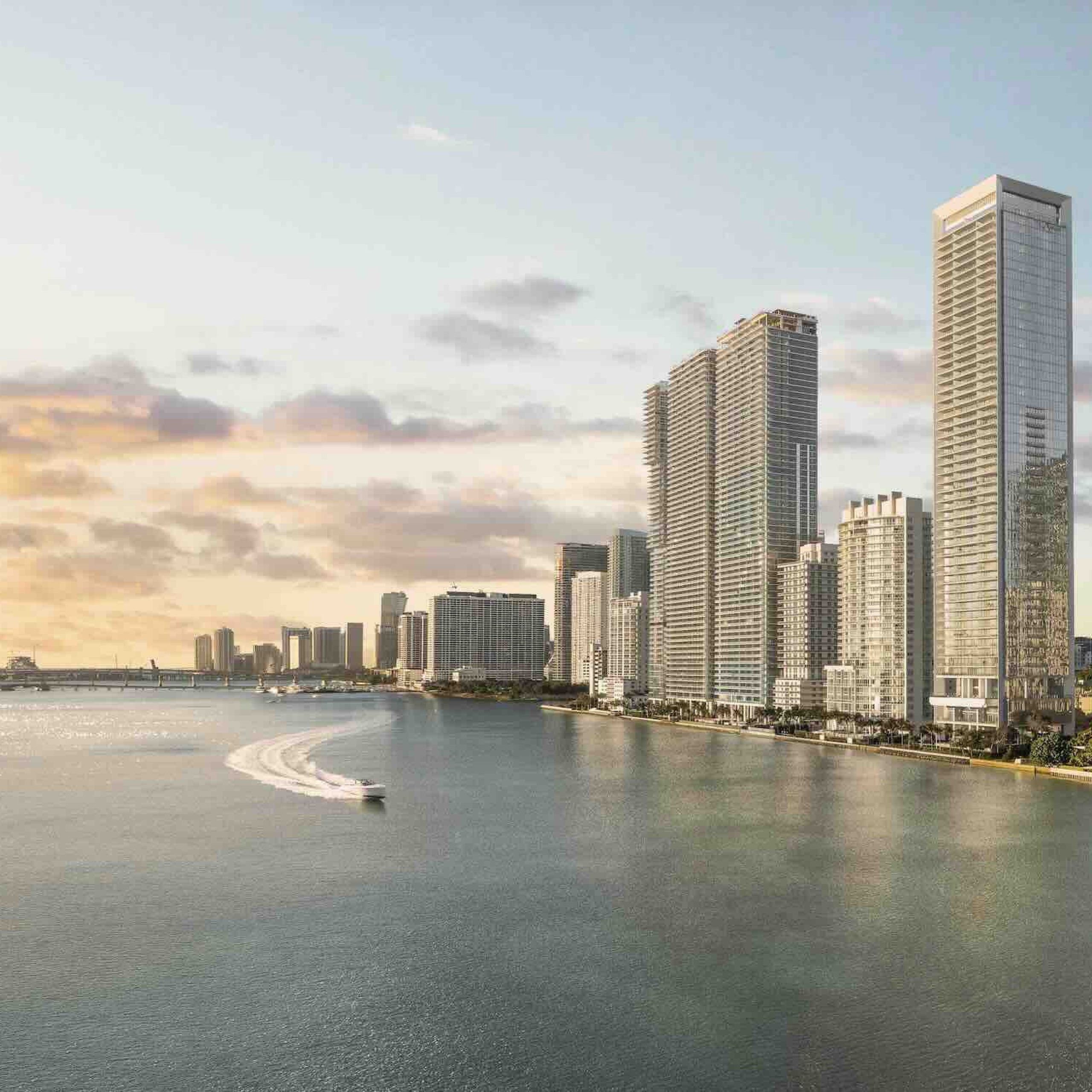 Miami's luxury waterfront skyline features modern high-rise buildings along the tranquil water at sunset.