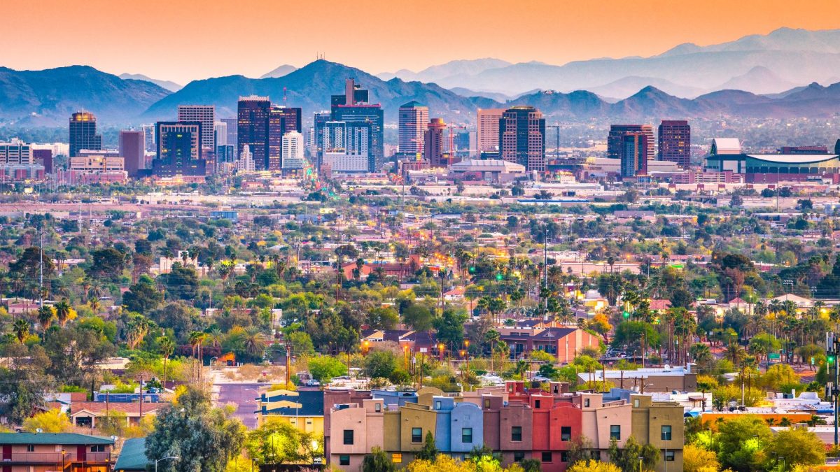 Panoramic view of downtown Phoenix with colorful buildings and mountains against a sunset sky.