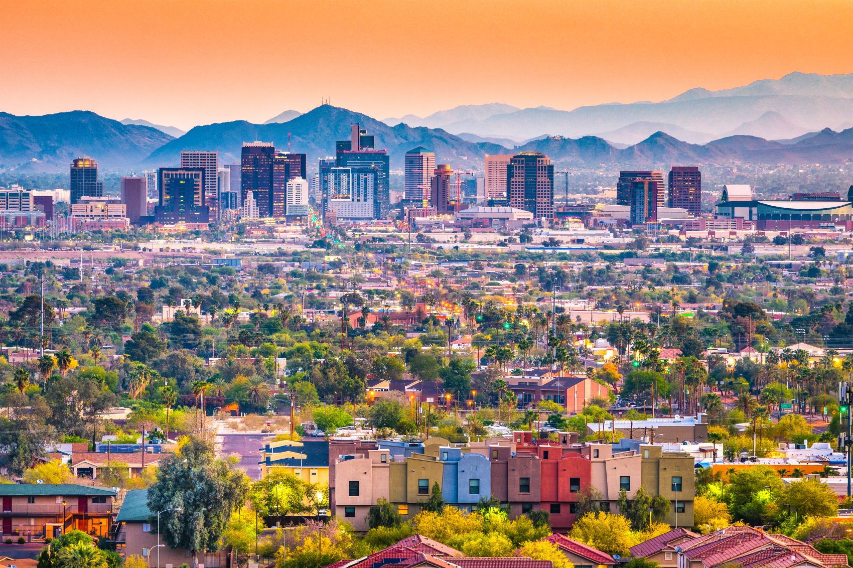 Panoramic view of downtown Phoenix with colorful buildings and mountains against a sunset sky.