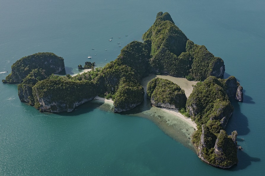 Aerial view of a lush, green island surrounded by clear blue water, ideal for sports and outdoor activities.