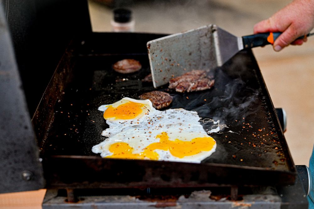 Outdoor grill with burgers and eggs cooking on a flattop surface
