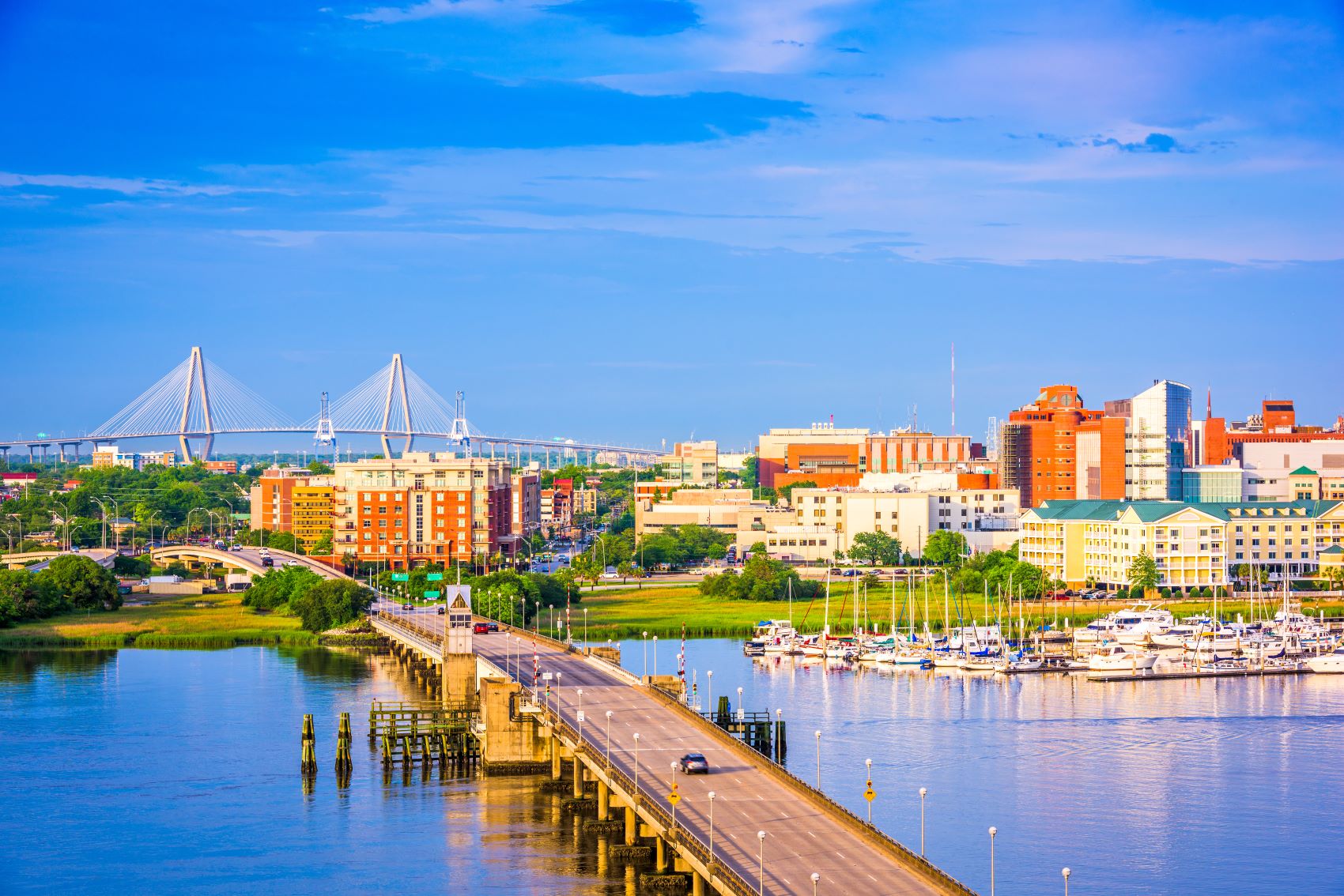 Charleston's skyline featuring a bridge, waterfront, and buildings with blue sky and water reflecting the vibrant scenery.
