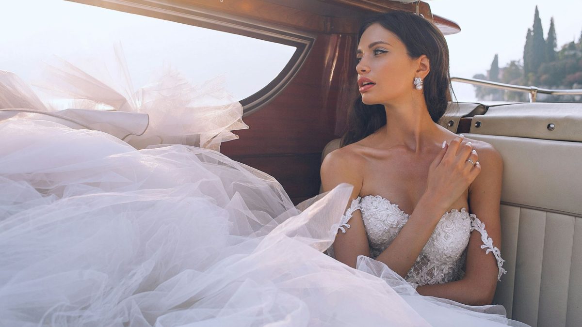 Bride in a luxurious wedding gown, seated elegantly in a boat, with soft tulle flowing around her and natural light highlighting her features.