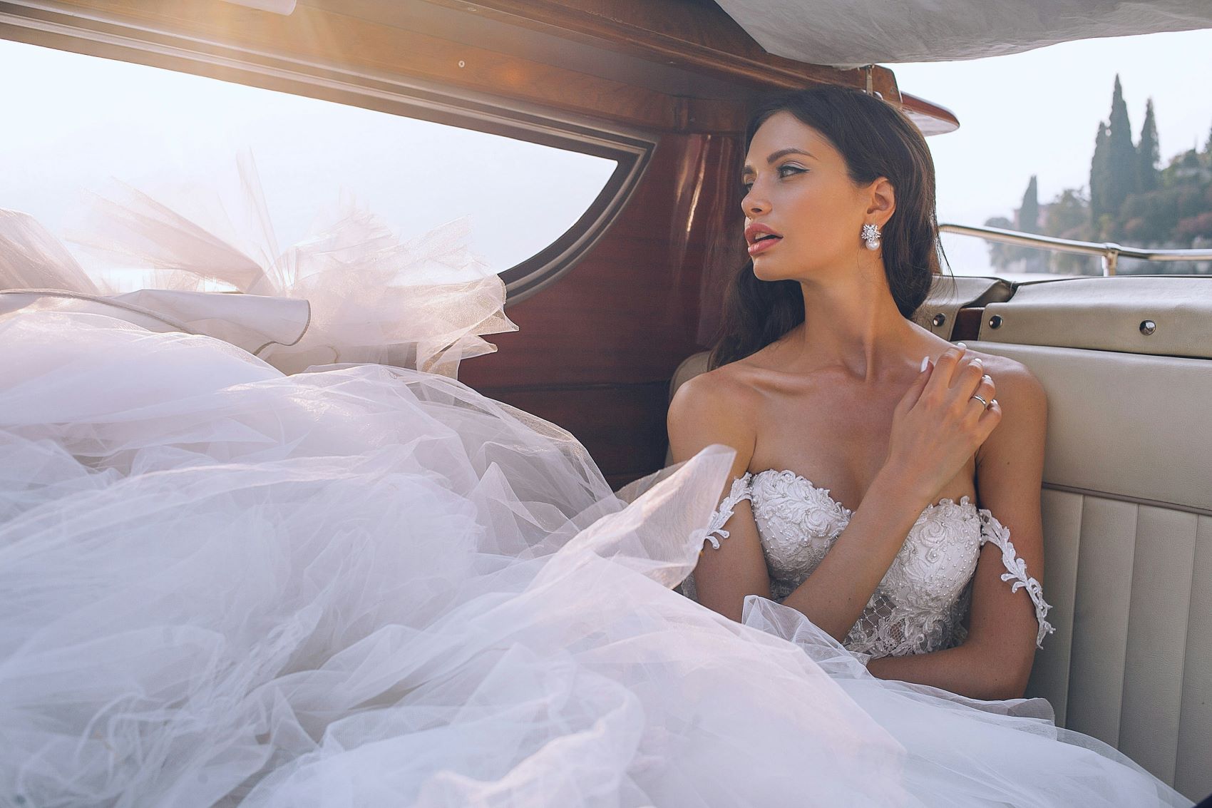 Bride in a luxurious wedding gown, seated elegantly in a boat, with soft tulle flowing around her and natural light highlighting her features.
