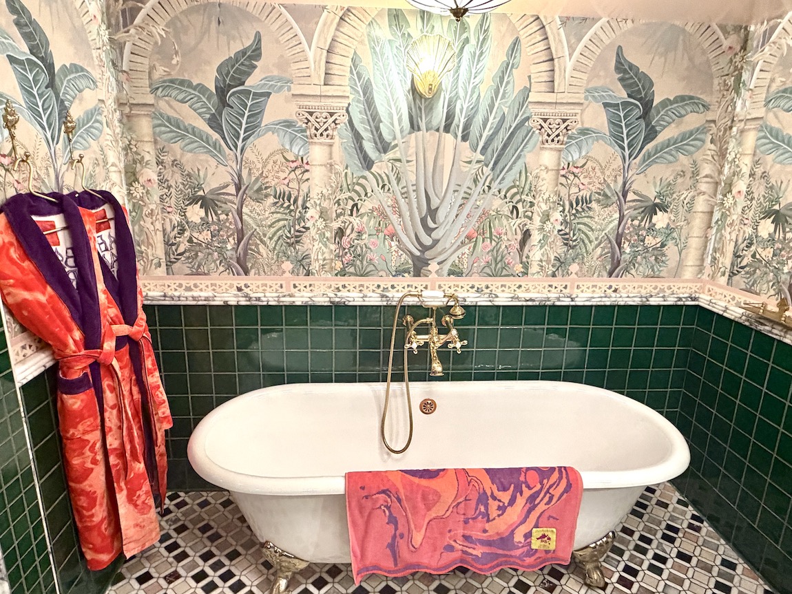 Luxurious bathroom at The Baby Grand in Coronado, featuring a vintage bathtub, colorful robe, and vibrant wallpaper.