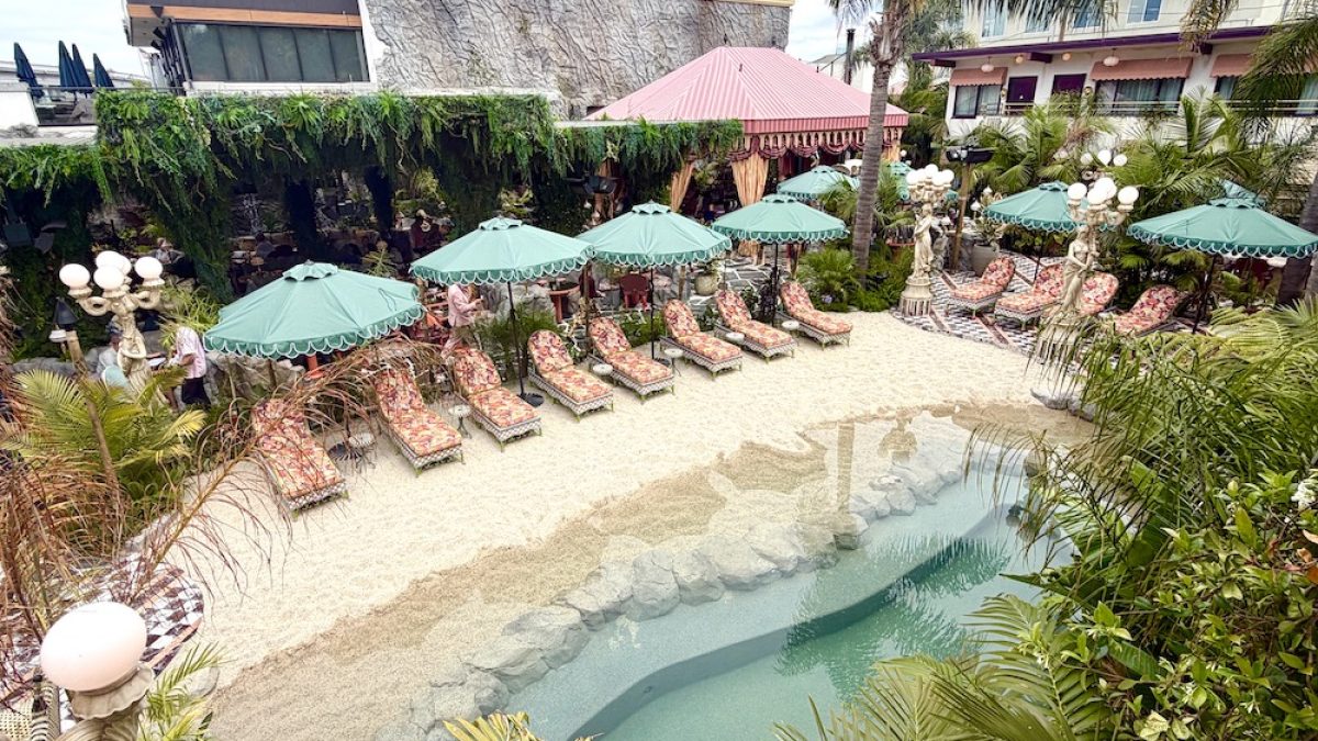 Tropical pool area at the Baby Grand, featuring lounge chairs, umbrellas, and a sandy beach surrounded by lush greenery.