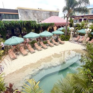 Tropical pool area at the Baby Grand, featuring lounge chairs, umbrellas, and a sandy beach surrounded by lush greenery.
