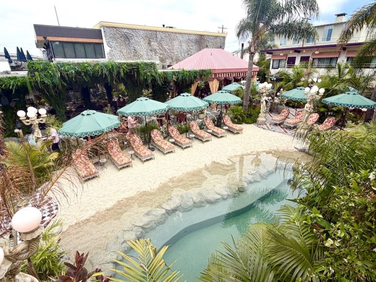 Tropical pool area at the Baby Grand, featuring lounge chairs, umbrellas, and a sandy beach surrounded by lush greenery.