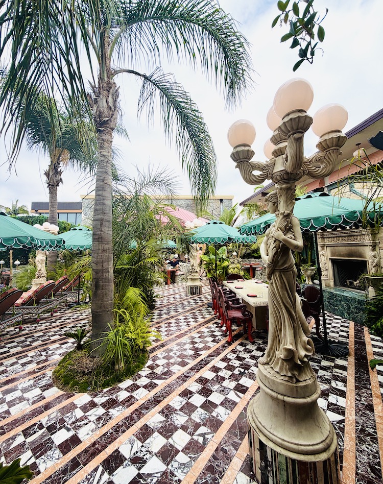 Stylish outdoor dining area at The Baby Grand in Coronado, featuring palm trees, a checkered floor, and an ornate lamp.
