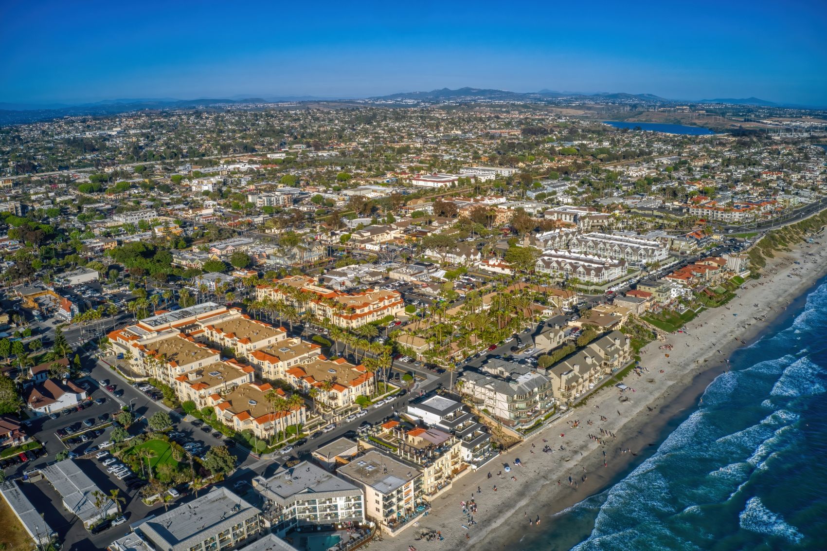 Aerial view of Carlsbad featuring beachfront property, residential areas, and vibrant urban landscape under a clear blue sky.