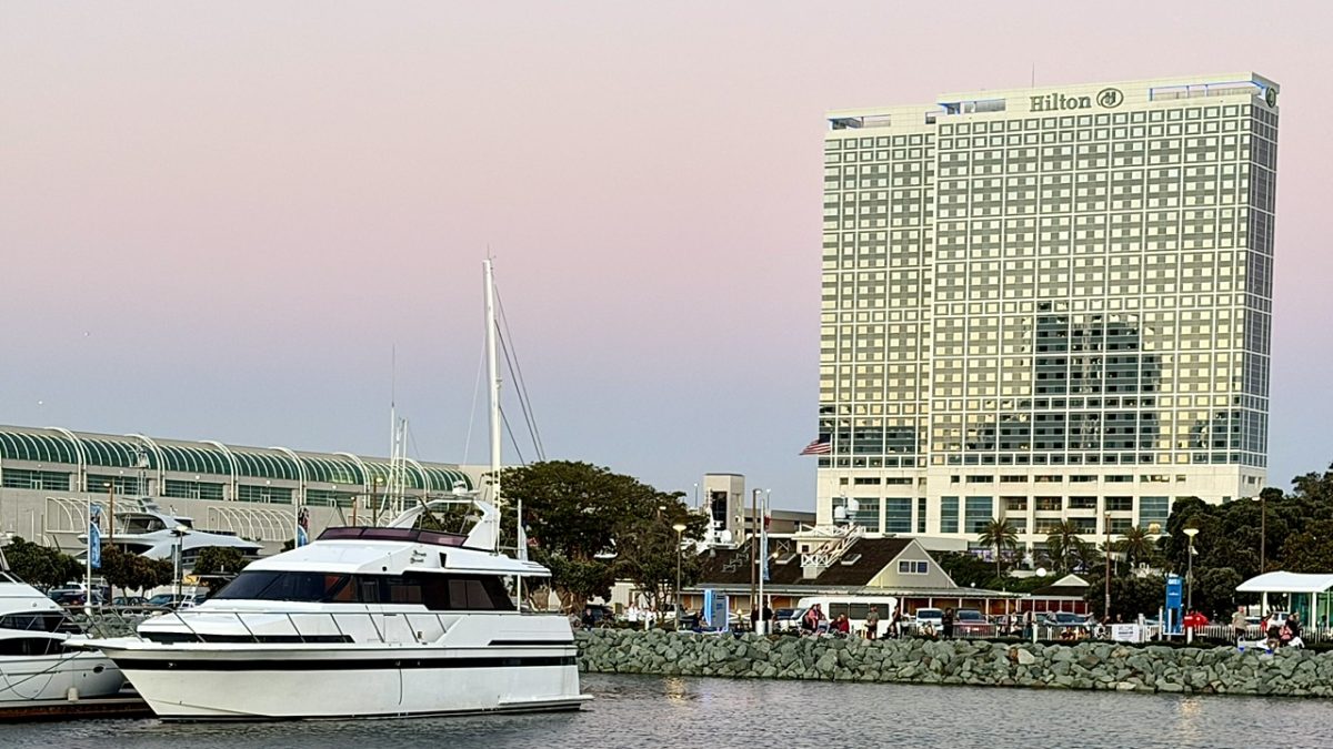 Hilton San Diego Bayfront hotel beside a marina with yachts, set against a pastel sunset sky.