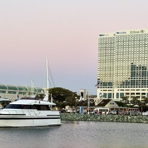 Hilton San Diego Bayfront hotel beside a marina with yachts, set against a pastel sunset sky.
