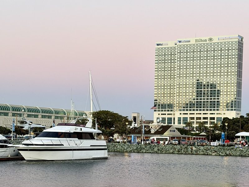 Hilton San Diego Bayfront hotel beside a marina with yachts, set against a pastel sunset sky.
