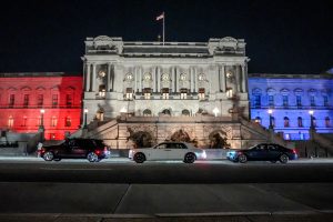 Three Rolls-Royce cars parked in front of a grand building illuminated in red, white, and blue for America's 250th anniversary.