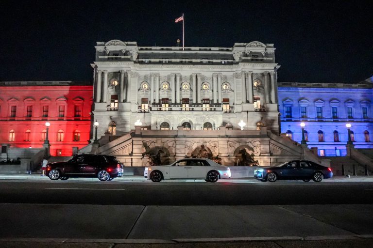 Three Rolls-Royce cars parked in front of a grand building illuminated in red, white, and blue for America's 250th anniversary.