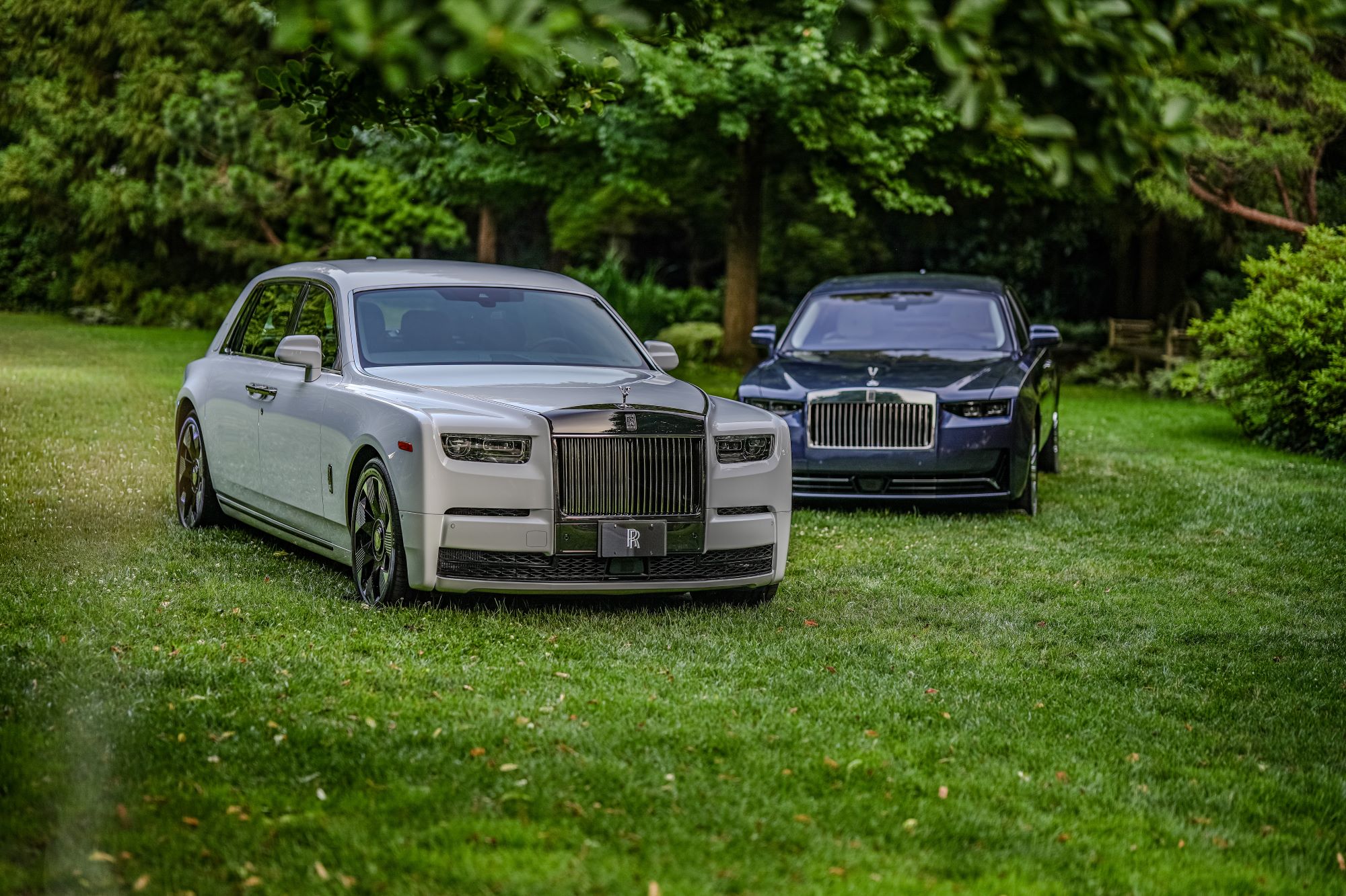 Two Rolls-Royce cars displayed on a grassy area, showcasing luxury design amidst lush greenery.