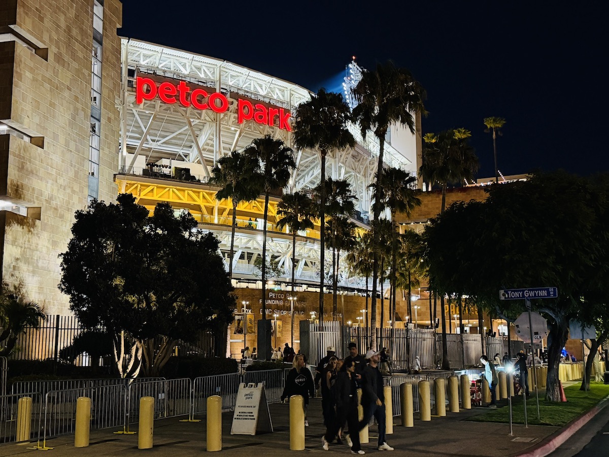 Petco Park illuminated at night with palm trees and fans arriving for a baseball game near the Hilton San Diego Bayfront.