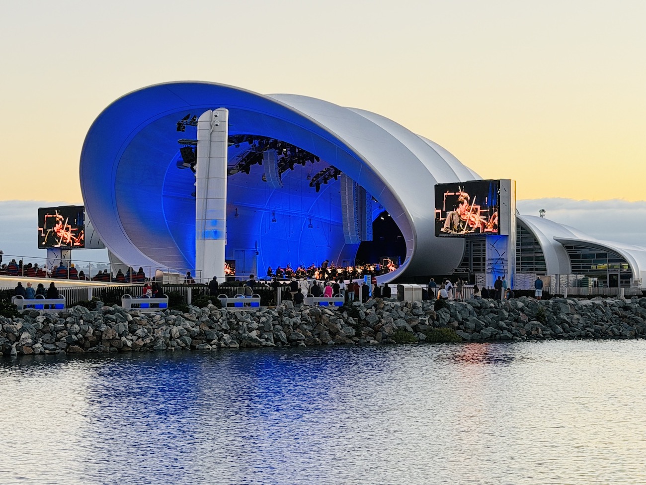 The Rady Shell at Jacobs Park, a modern outdoor concert venue with blue lighting and screens, located by the waterfront.