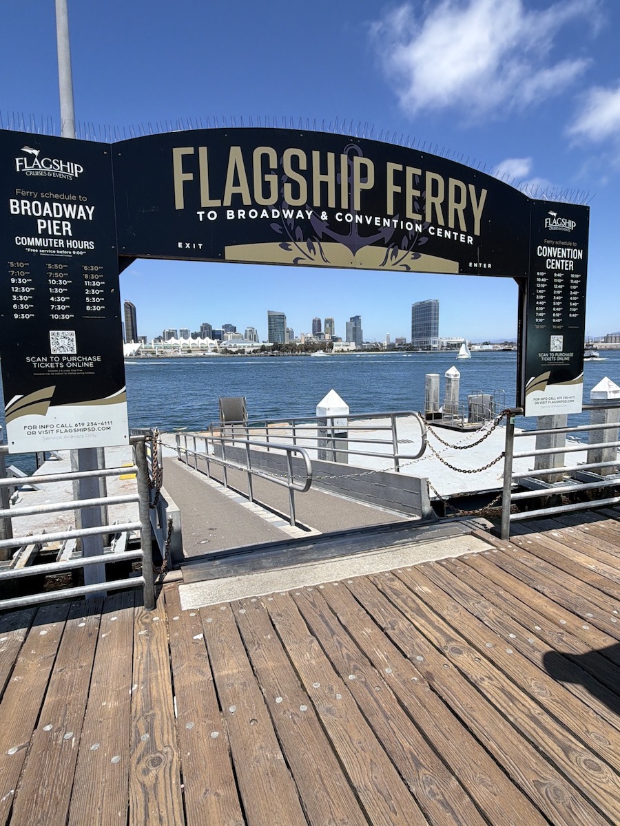 Flagship Ferry sign at Broadway Pier with San Diego skyline and calm water in the background, inviting commuters to board.