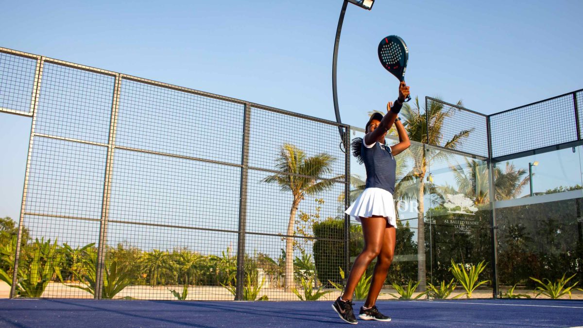 A player prepares to hit a padel ball on a court surrounded by palm trees at Al Baleed Resort in Salalah.