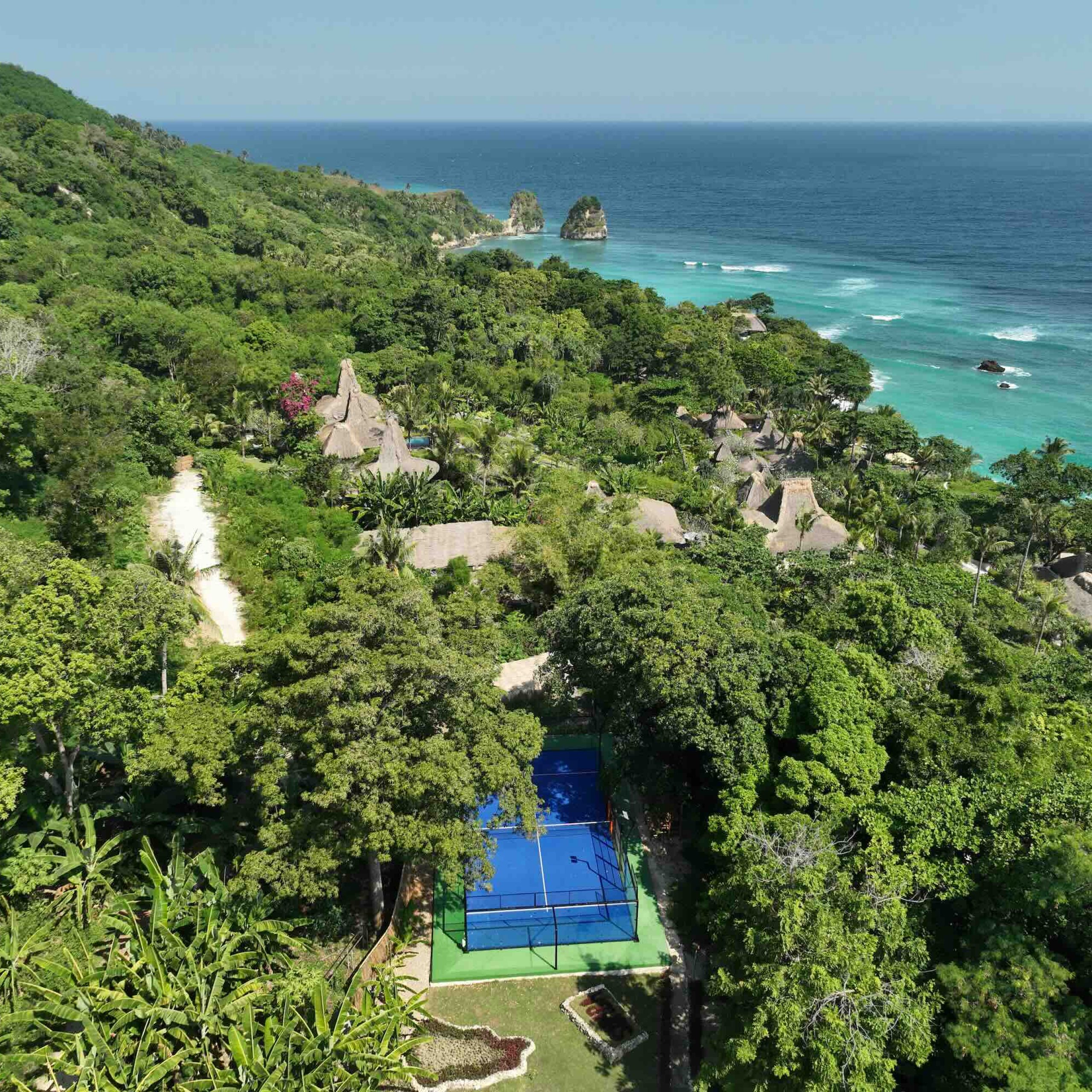 Lush green landscape with a blue padel court overlooking the ocean, showcasing the luxury of Privé Padel's travel experience.