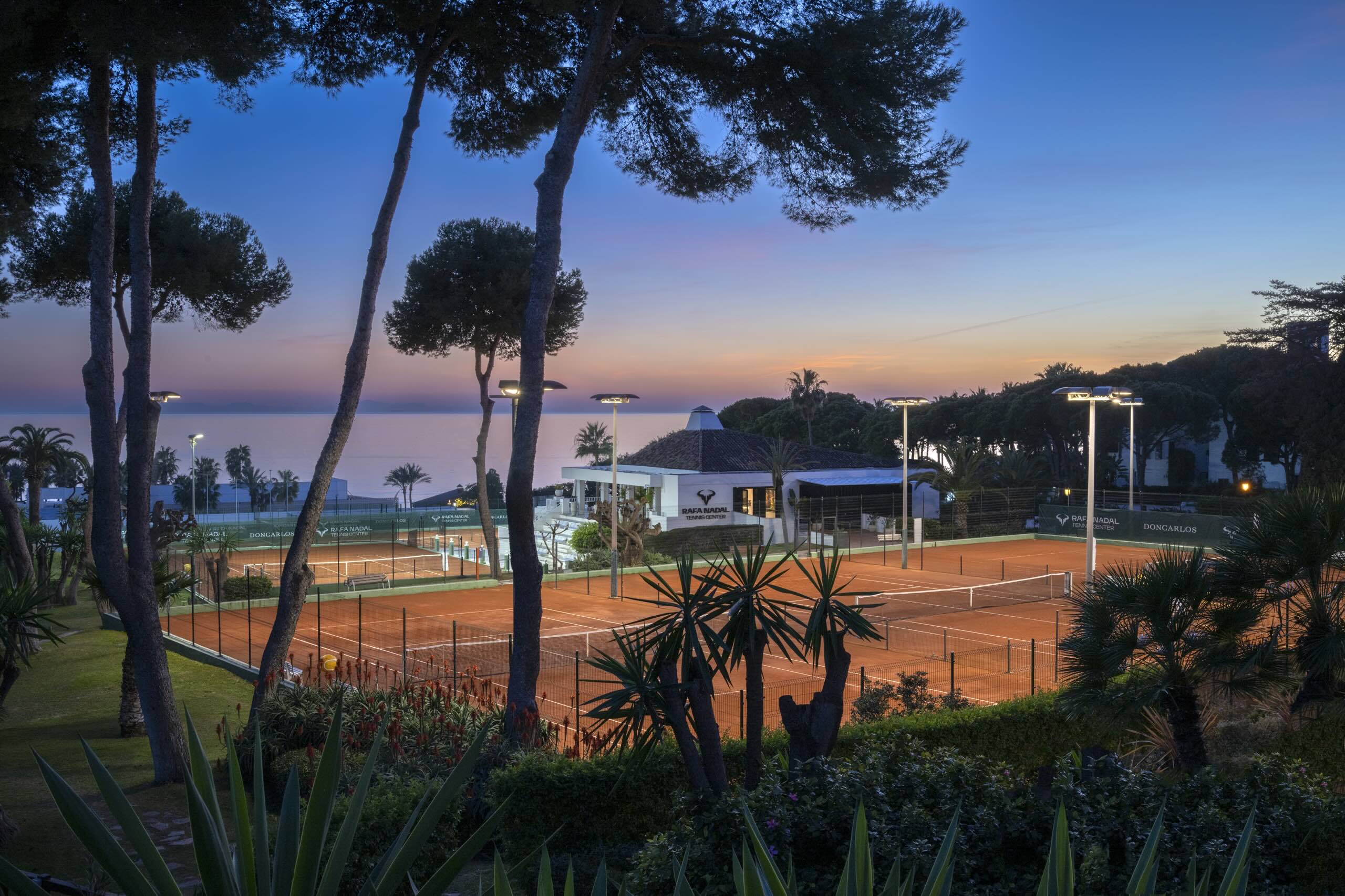 Tennis courts with palm trees and ocean views at sunset, highlighting the luxury of Privé Padel in Marbella.