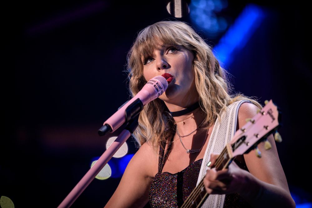 Taylor Swift performing on stage with a guitar and pink microphone, showcasing her evolved style and confidence.