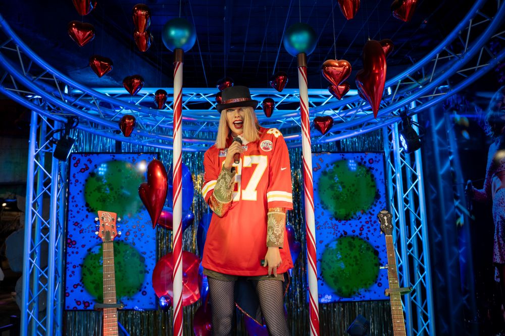 Stylishly dressed performer in a red jersey poses in a colorful backdrop with hearts and guitars, capturing a vibrant atmosphere.