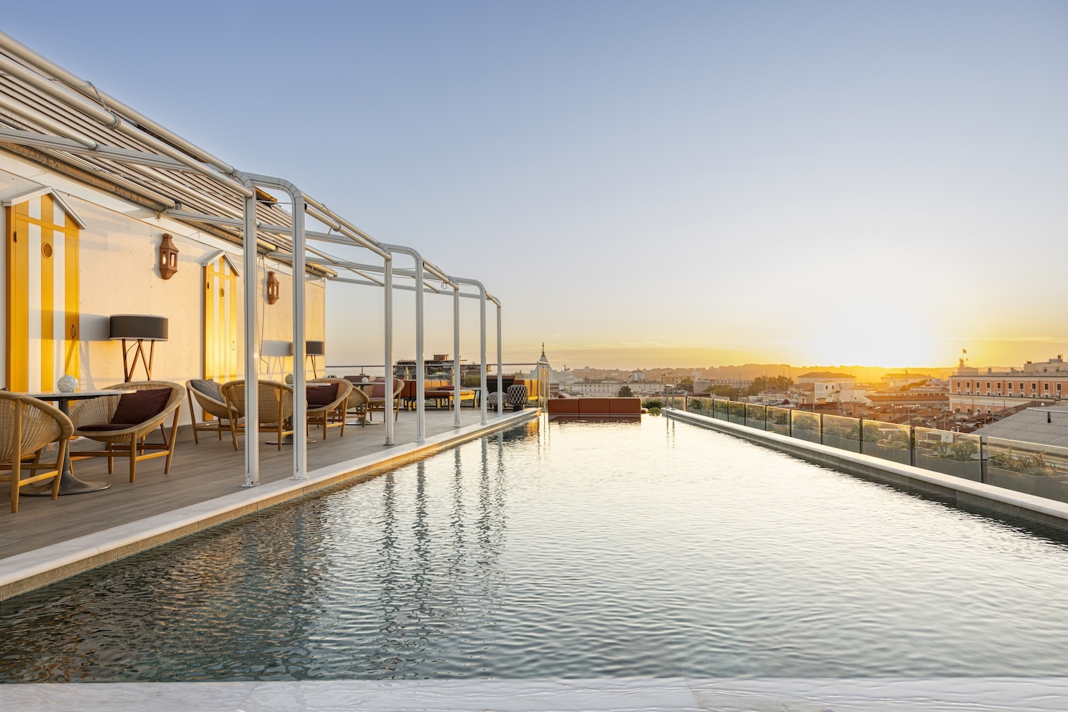 Rooftop pool with modern seating offers a stunning view of the sunset over Rome's skyline.