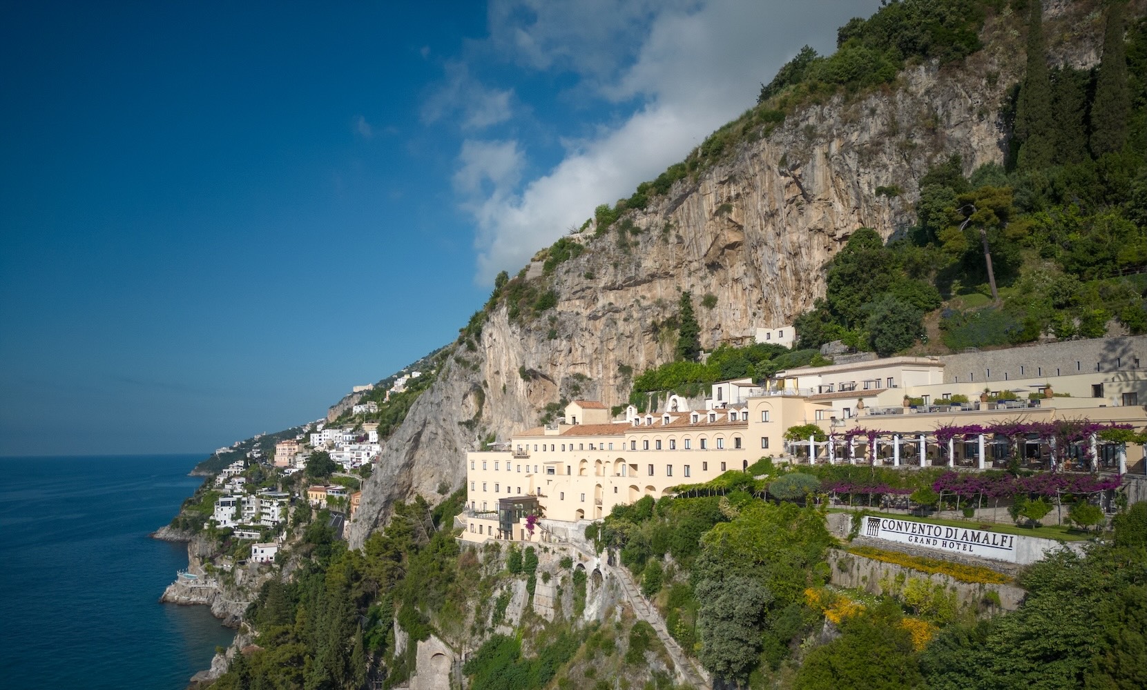 Aerial view of Convento di Amalfi Grand Hotel nestled against a cliff overlooking the Amalfi Coast and the Mediterranean Sea.