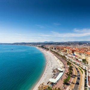 Aerial view of Nice's Promenade with blue waters, sandy beaches, and vibrant city buildings under a clear sky.
