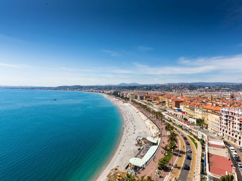 Aerial view of Nice's Promenade with blue waters, sandy beaches, and vibrant city buildings under a clear sky.