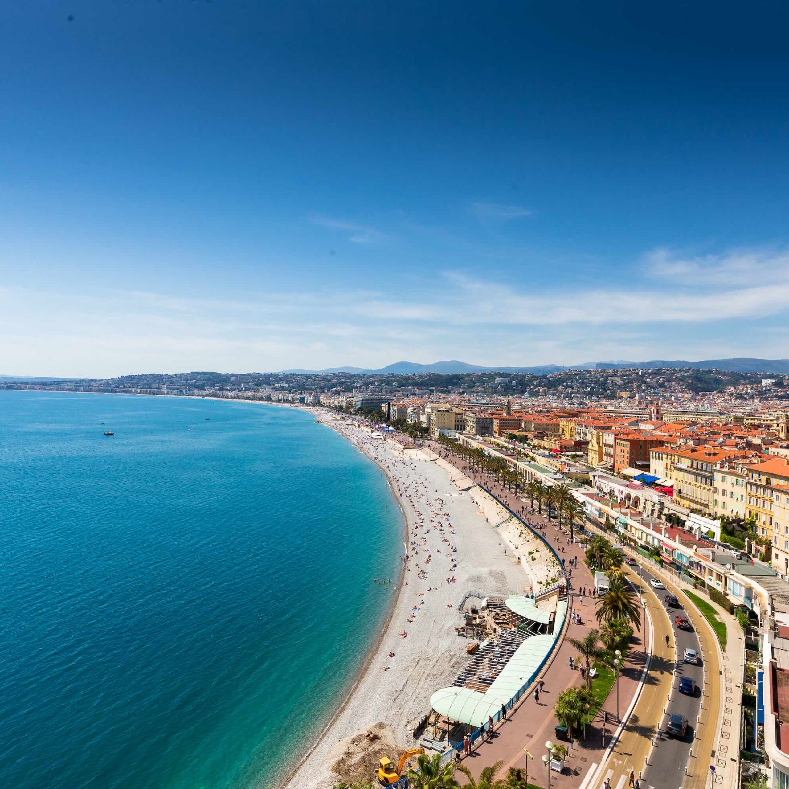 Aerial view of Nice's Promenade with blue waters, sandy beaches, and vibrant city buildings under a clear sky.