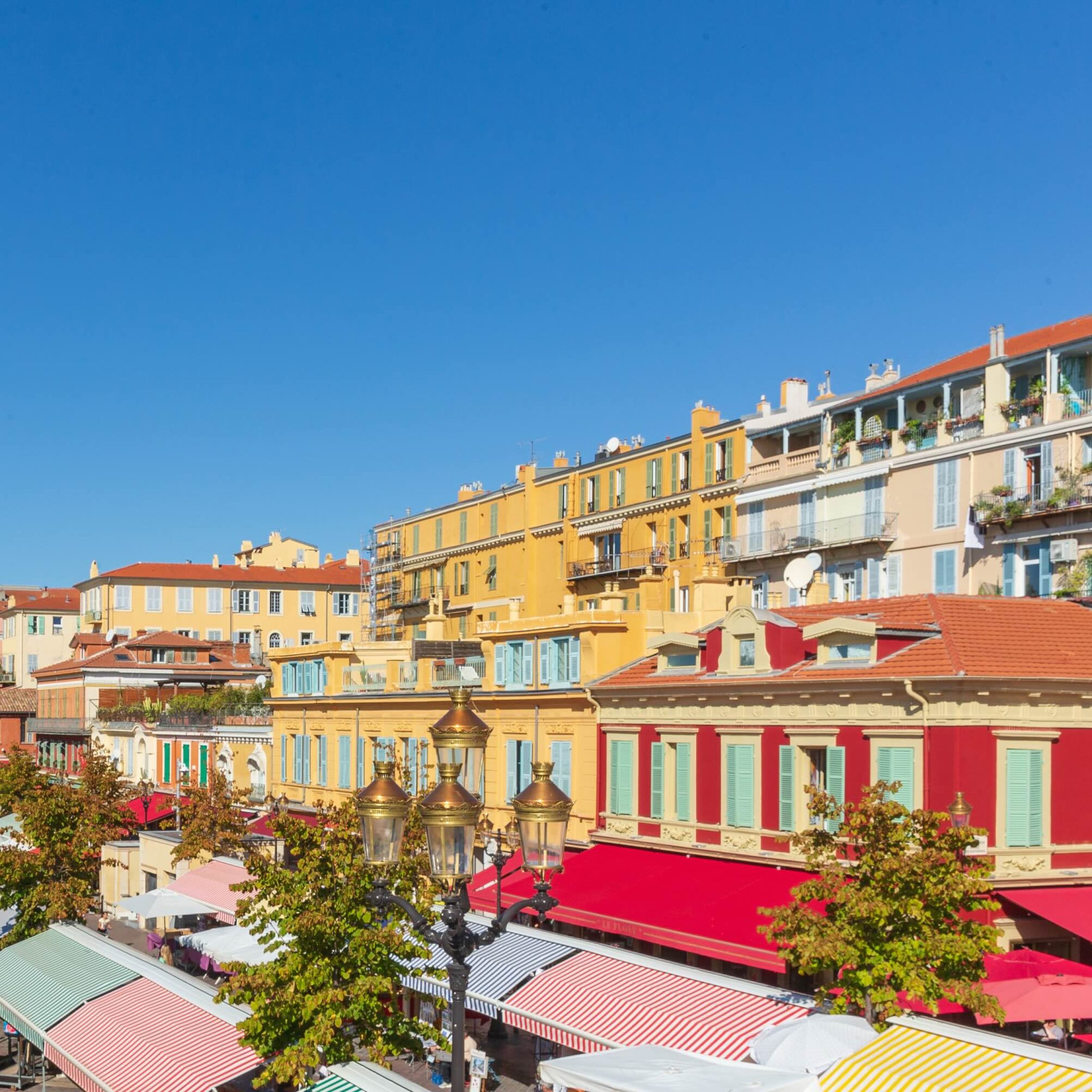 Lively marketplace with colorful buildings and awnings under a clear blue sky, inviting visitors to explore the area.