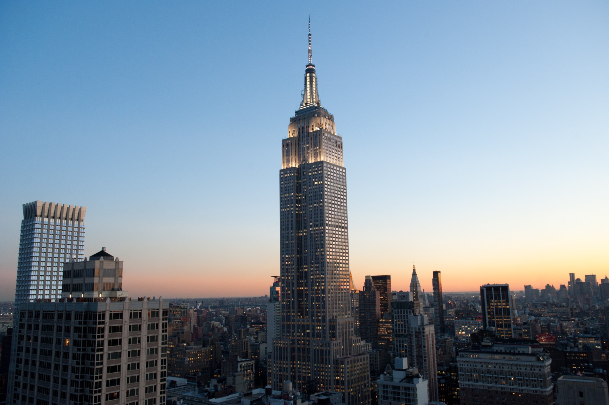 The Empire State Building illuminated against a twilight sky, showcasing its iconic Art Deco architecture amidst the New York City skyline.