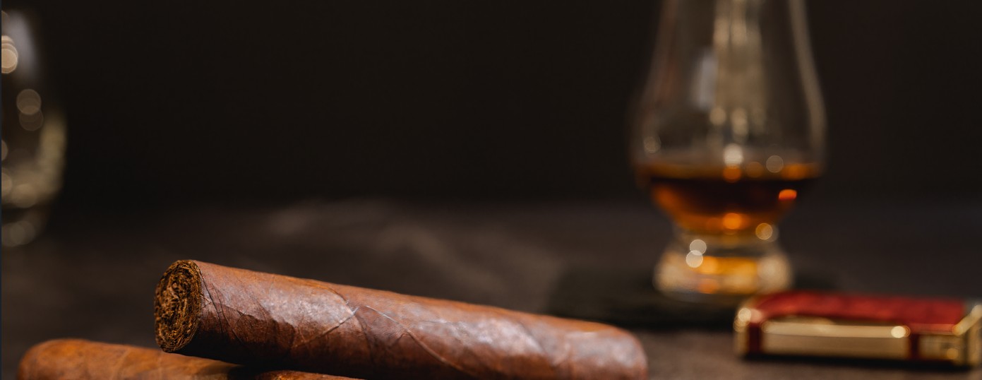 Premium cigars laid on a table beside a glass of whiskey and a lighter, evoking a luxurious smoking experience.