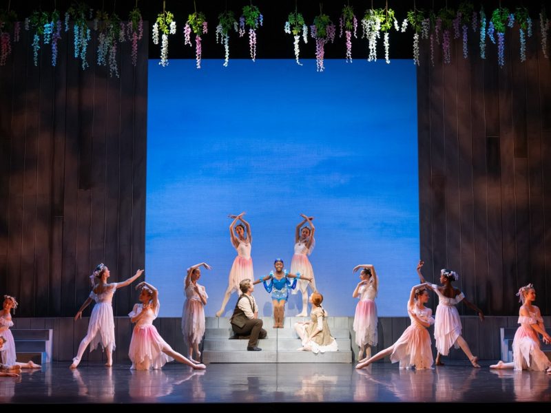 Dancers performing a scene from Anne of Green Gables at the Peacock Theatre, featuring floral decorations and a vibrant backdrop.