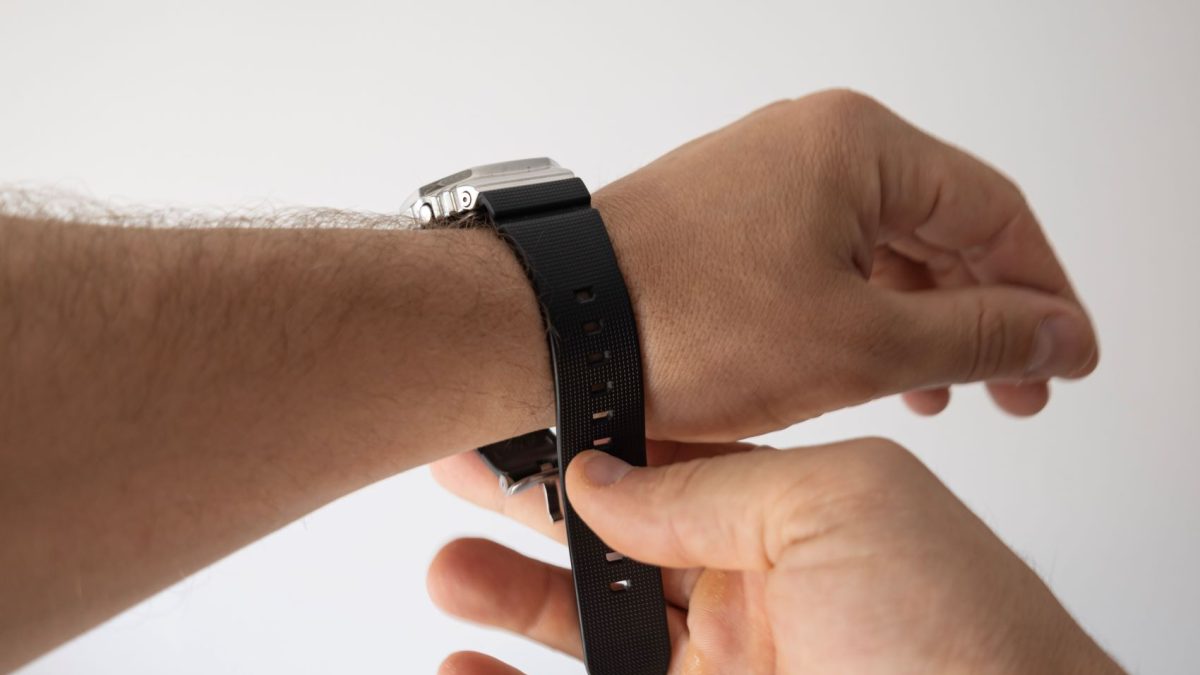 A person adjusts a black rubber strap on a luxury watch worn on their wrist.