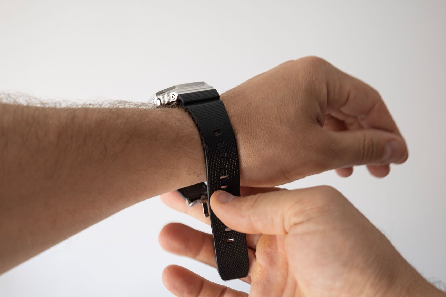 A person adjusts a black rubber strap on a luxury watch worn on their wrist.