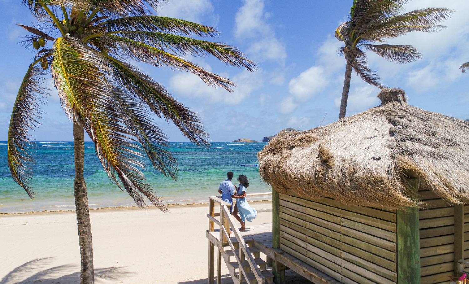Couple enjoying a romantic moment near a beach cabana, surrounded by palm trees and ocean waves.